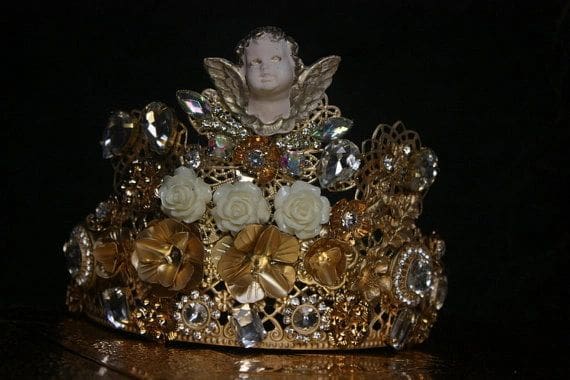 A gold crown with a white angel on top of it.
