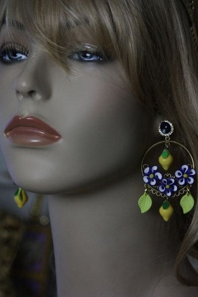 A woman wearing earrings with blue flowers and green leaves.
