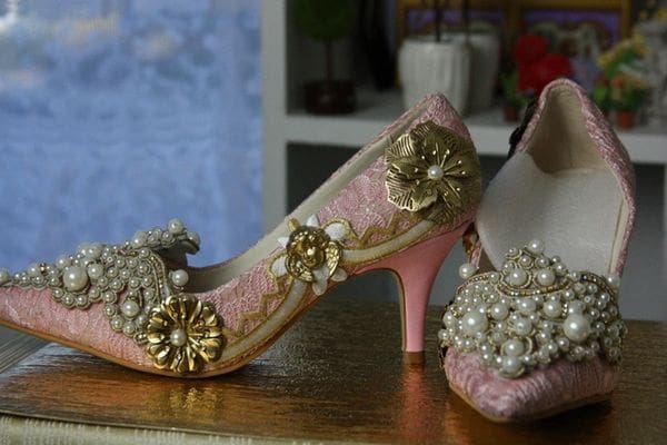 A pair of pink and gold shoes with pearls on top.