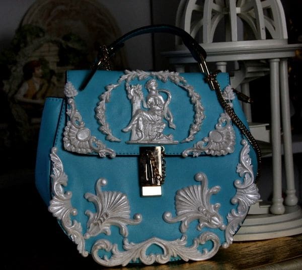 A blue purse with silver trim and white designs.