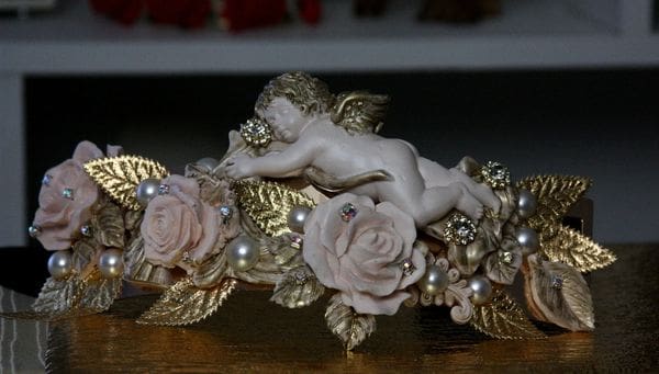 A statue of a cherub with roses and pearls.