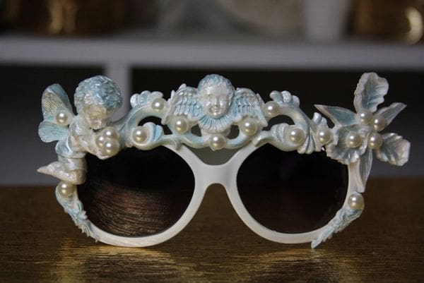 A pair of white sunglasses with pearls and angels on it.