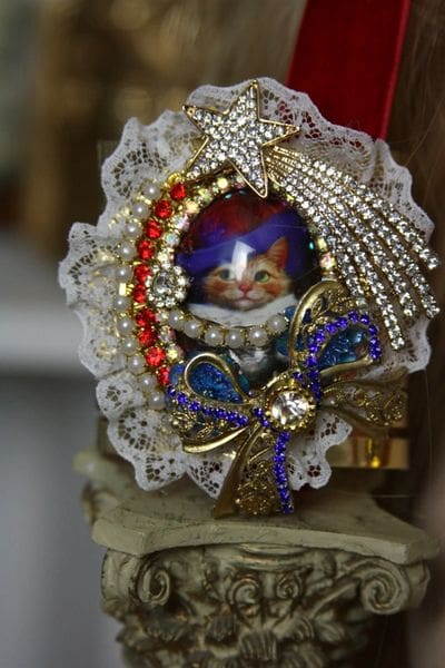 A cat ornament with lace and beads on top of it.