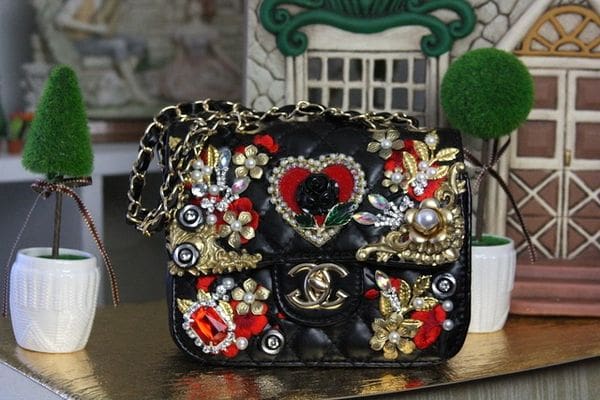 A black purse with gold chain and red heart on it.