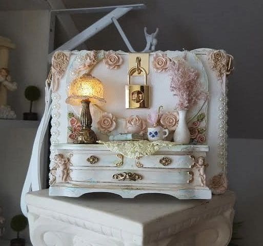 A white dresser with a lamp and vase on top of it.