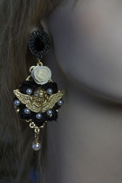 A woman wearing black and gold earrings with white rose.