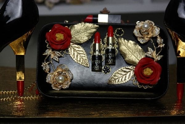 A black purse with gold leaves and red lipstick.