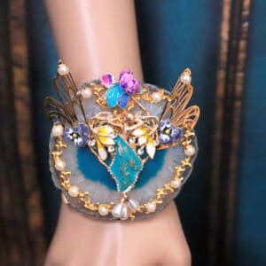 A woman 's hand wearing a bracelet with pearls and blue stones.
