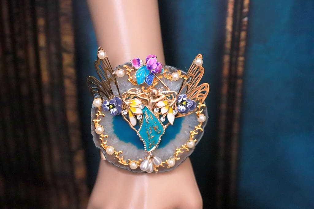 A woman 's hand wearing a bracelet with pearls and blue stones.