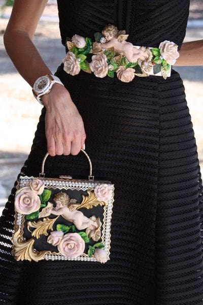 A woman holding onto a black purse with pink flowers