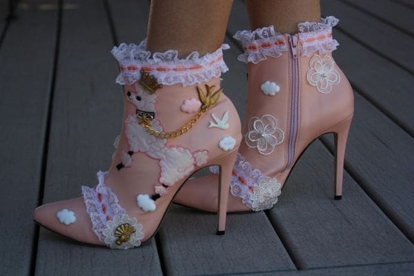 A person wearing pink shoes with lace and pearls.